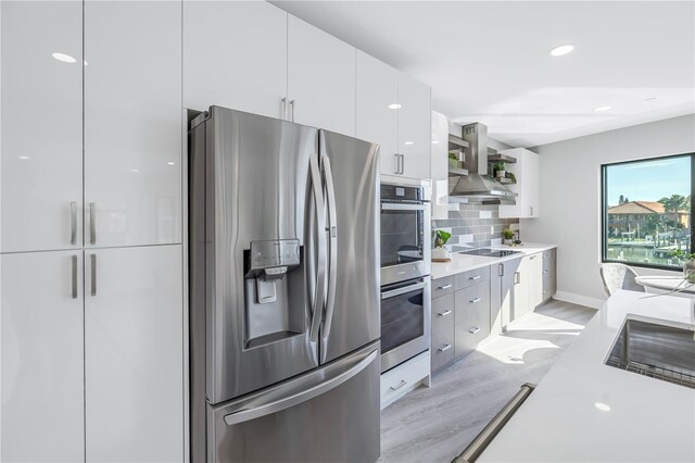 kitchen with stainless steel appliances, light countertops, backsplash, wall chimney exhaust hood, and modern cabinets