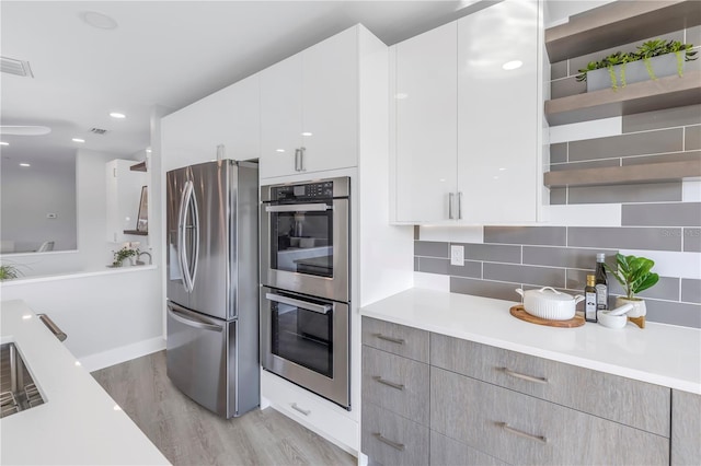 kitchen with tasteful backsplash, modern cabinets, appliances with stainless steel finishes, light countertops, and light wood-type flooring