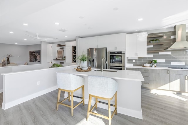 kitchen with stainless steel appliances, a sink, wall chimney range hood, light wood-type flooring, and modern cabinets