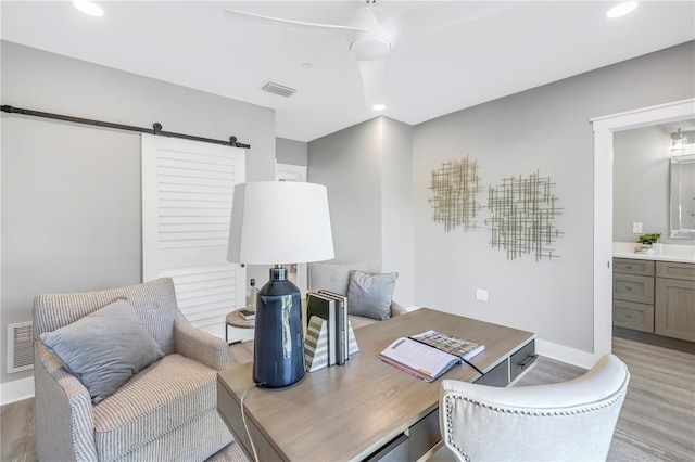 office featuring a barn door, light wood-type flooring, visible vents, and recessed lighting