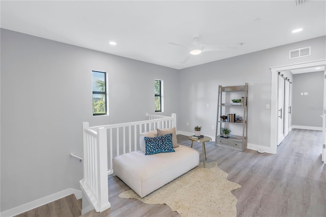 sitting room with light wood-type flooring, baseboards, visible vents, and an upstairs landing