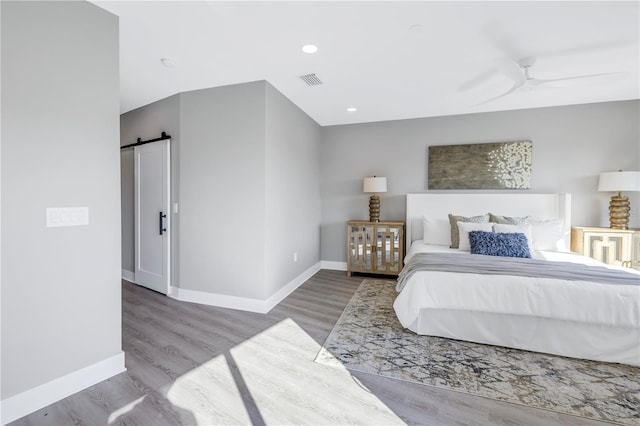 bedroom with baseboards, a barn door, visible vents, and wood finished floors