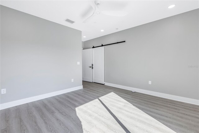 unfurnished bedroom with a barn door, wood finished floors, visible vents, and baseboards