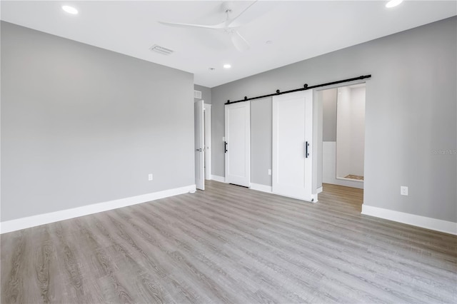 unfurnished bedroom with recessed lighting, visible vents, a barn door, light wood-type flooring, and baseboards