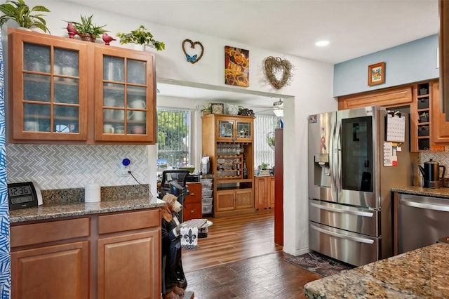 kitchen with appliances with stainless steel finishes, dark stone countertops, backsplash, and dark hardwood / wood-style flooring