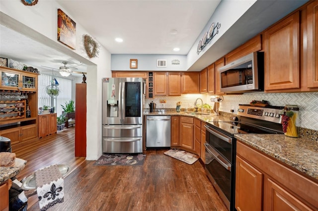 kitchen with light stone countertops, appliances with stainless steel finishes, dark wood-type flooring, sink, and ceiling fan