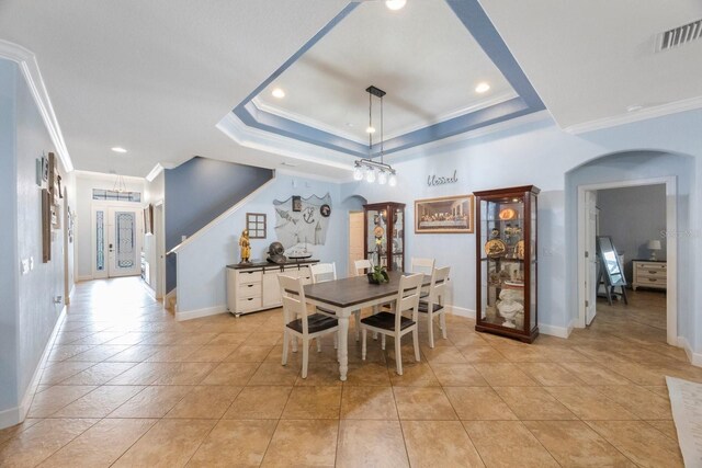 tiled dining area featuring ornamental molding and a tray ceiling