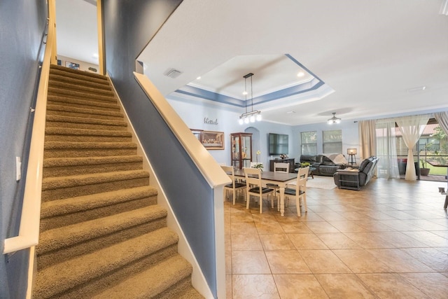 stairway featuring ornamental molding, tile patterned flooring, a tray ceiling, and ceiling fan