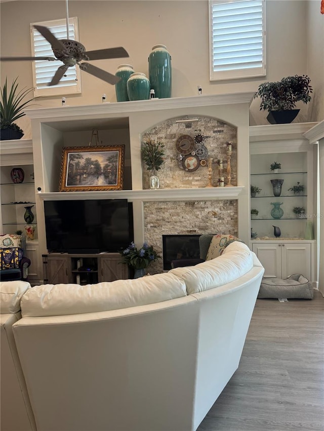 living room featuring built in features, a fireplace, ceiling fan, and wood finished floors