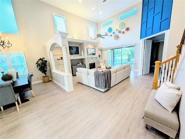 living room with crown molding, stairs, ceiling fan with notable chandelier, a fireplace, and wood finished floors