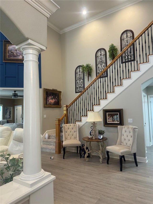 stairway with crown molding, baseboards, a towering ceiling, wood finished floors, and ornate columns