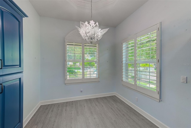 unfurnished dining area with a healthy amount of sunlight, baseboards, an inviting chandelier, and wood finished floors