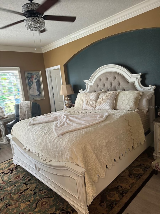 bedroom featuring a ceiling fan, a textured ceiling, wood finished floors, and crown molding