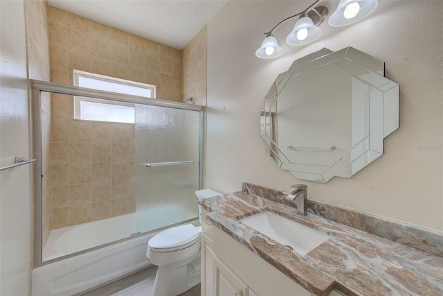 full bathroom with combined bath / shower with glass door, toilet, and vanity