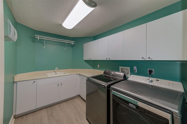 laundry area with light wood-style flooring, cabinet space, a sink, a textured ceiling, and washer and dryer