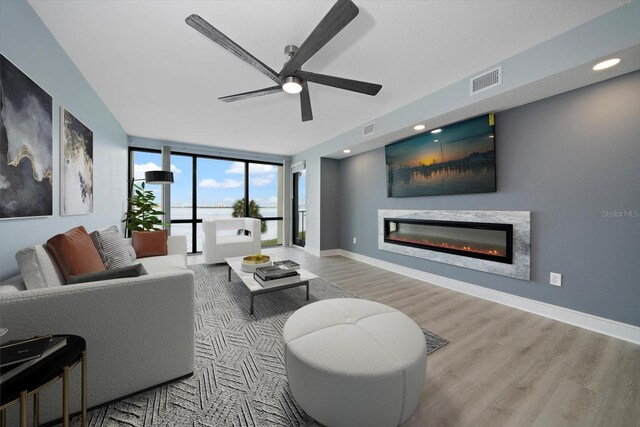 living room with ceiling fan, expansive windows, and light hardwood / wood-style flooring