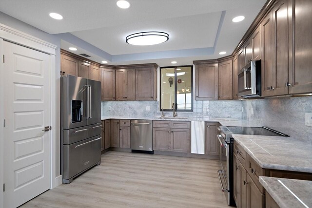 kitchen featuring backsplash, light wood-type flooring, appliances with stainless steel finishes, sink, and a tray ceiling