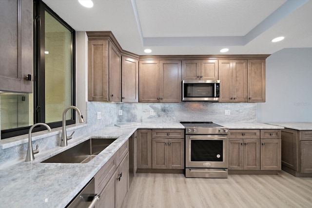 kitchen with light stone counters, stainless steel appliances, sink, and light hardwood / wood-style floors