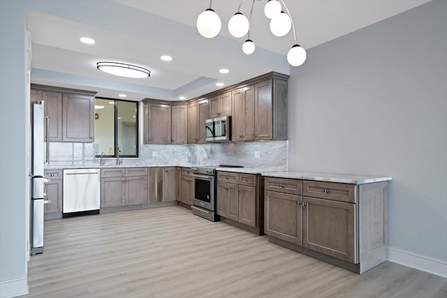 kitchen with tasteful backsplash, stainless steel appliances, hanging light fixtures, a raised ceiling, and light hardwood / wood-style floors