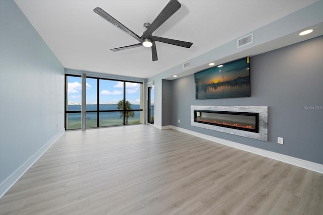 unfurnished living room with a high end fireplace, light hardwood / wood-style floors, ceiling fan, a water view, and floor to ceiling windows