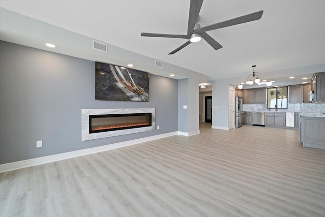 unfurnished living room featuring ceiling fan with notable chandelier, hardwood / wood-style flooring, and a fireplace