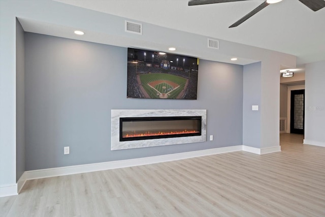 unfurnished living room featuring a premium fireplace, hardwood / wood-style flooring, and ceiling fan