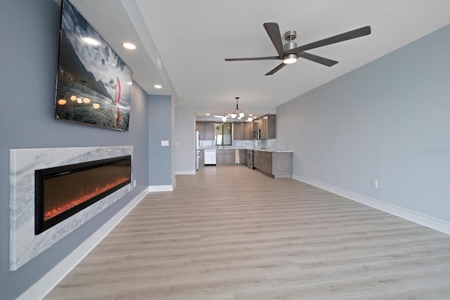 unfurnished living room featuring light hardwood / wood-style flooring, ceiling fan with notable chandelier, and a fireplace