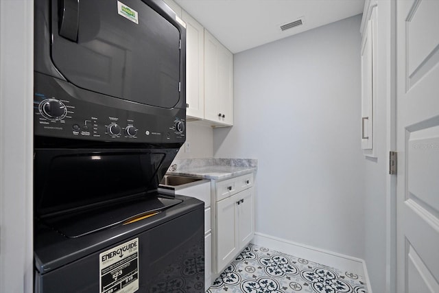 laundry room featuring light tile patterned floors, cabinets, and stacked washer / dryer