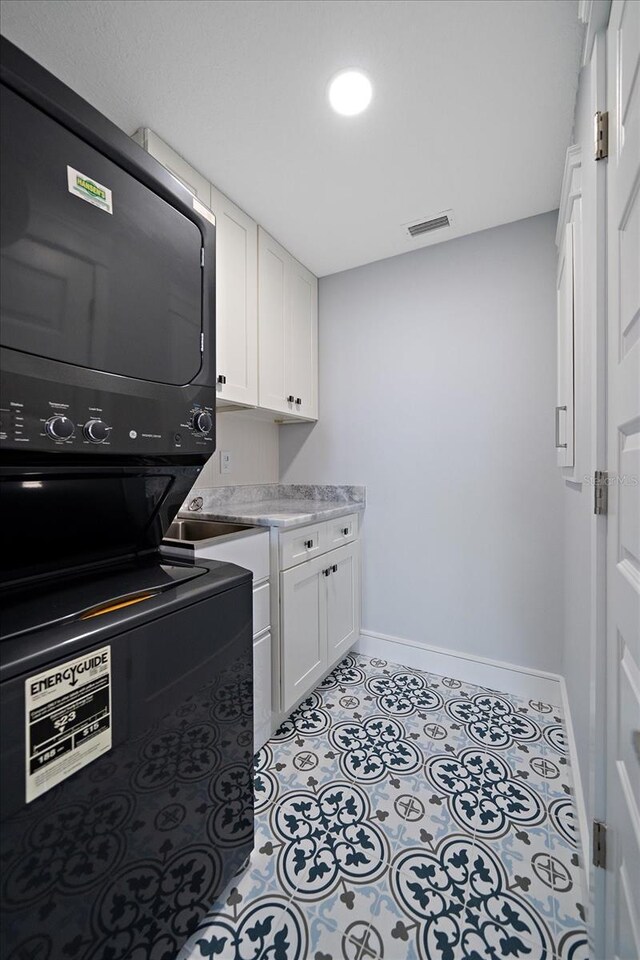 laundry room featuring cabinets and stacked washer / dryer