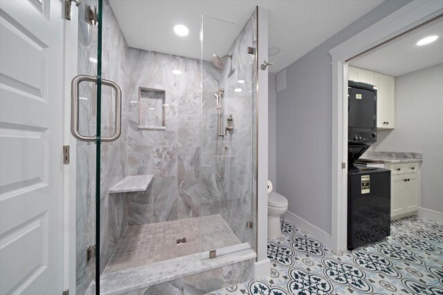 bathroom featuring toilet, stacked washer and dryer, tile patterned floors, vanity, and a shower with shower door