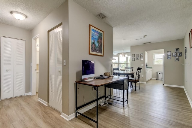 office space with light wood-type flooring, a notable chandelier, and a textured ceiling