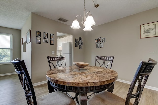 dining area featuring a chandelier, light hardwood / wood-style floors, and a textured ceiling