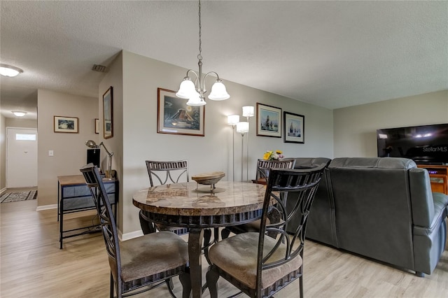 dining area featuring a textured ceiling, light hardwood / wood-style flooring, and a chandelier