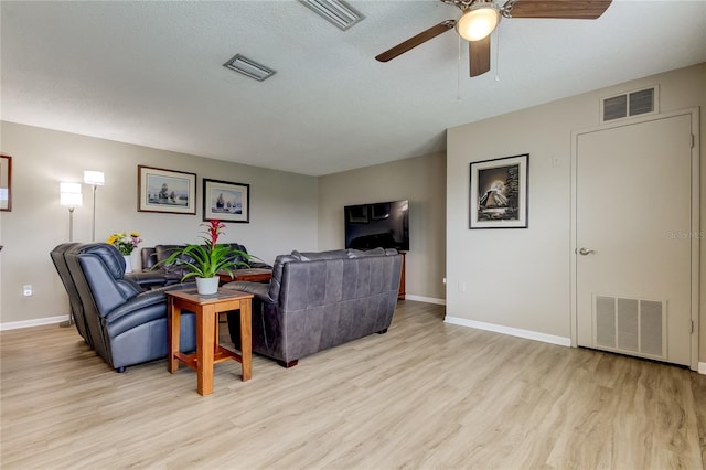 living room featuring light wood-type flooring, ceiling fan, and a textured ceiling