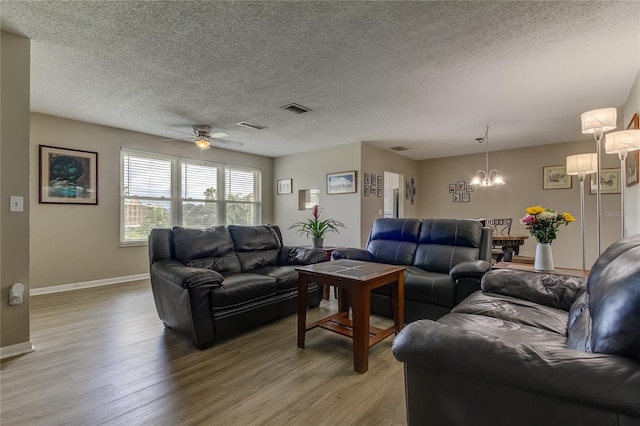 living room featuring light wood-type flooring, ceiling fan with notable chandelier, and a textured ceiling