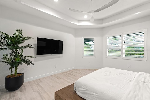 bedroom with light wood-type flooring, a tray ceiling, and ceiling fan