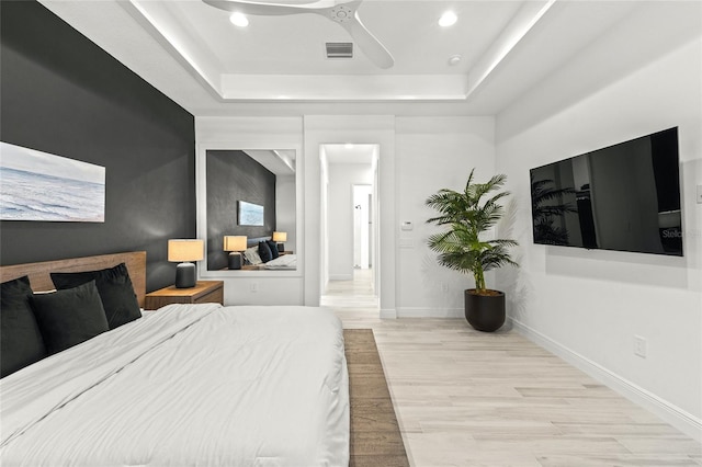 bedroom with light wood-type flooring, a tray ceiling, and ceiling fan