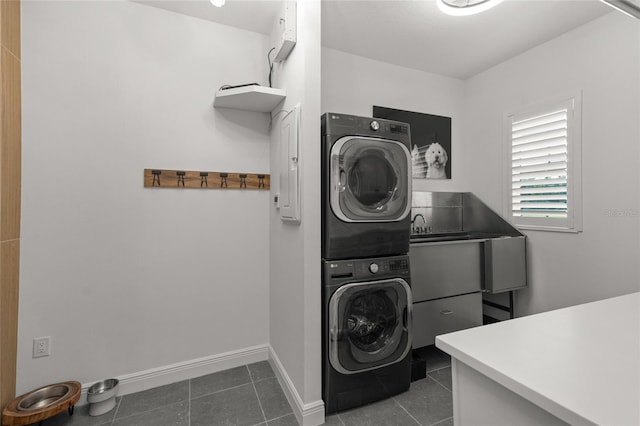 washroom featuring dark tile patterned flooring, stacked washing maching and dryer, and cabinets