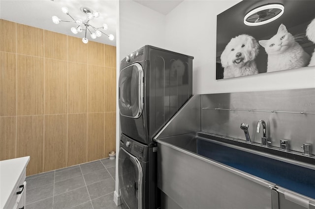 laundry area featuring tile walls, stacked washer and dryer, a notable chandelier, and tile patterned floors