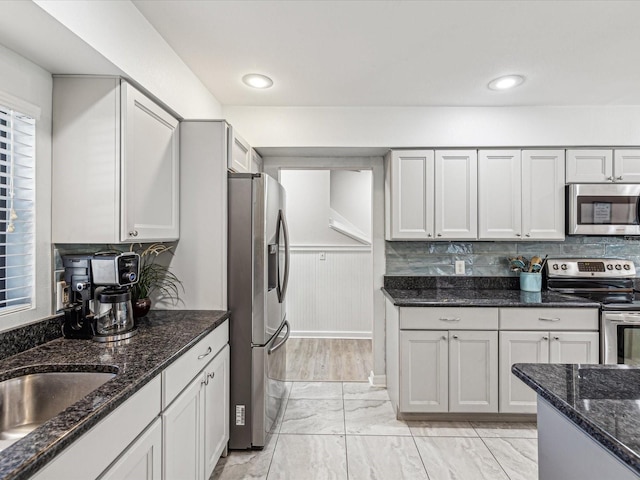 kitchen featuring tasteful backsplash, dark stone countertops, sink, white cabinetry, and appliances with stainless steel finishes