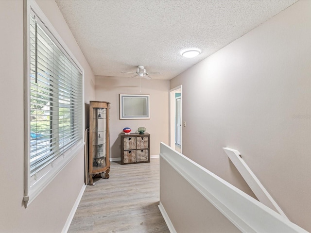 hallway with light wood-type flooring and a textured ceiling