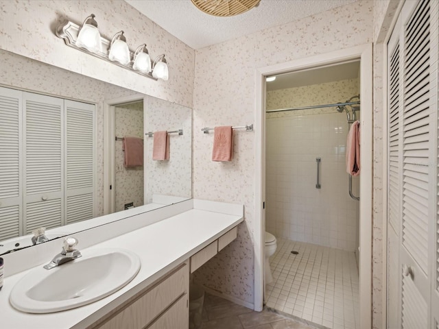 bathroom featuring a textured ceiling, vanity, a tile shower, tile patterned flooring, and toilet