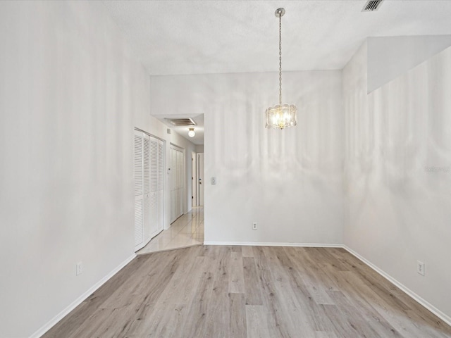 empty room with an inviting chandelier and light hardwood / wood-style flooring