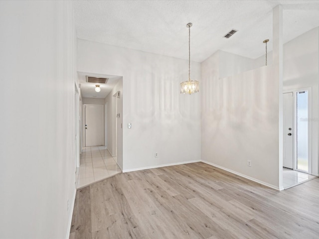 spare room with a notable chandelier, a textured ceiling, and light wood-type flooring