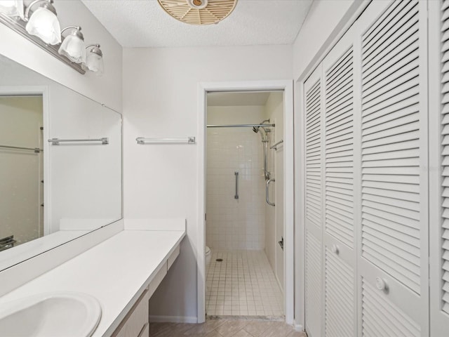 bathroom featuring tile patterned floors, toilet, a textured ceiling, a tile shower, and vanity