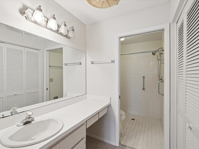 bathroom with tile patterned flooring, a tile shower, vanity, a textured ceiling, and toilet