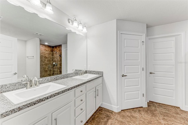 bathroom featuring tile patterned flooring, a tile shower, vanity, and a textured ceiling