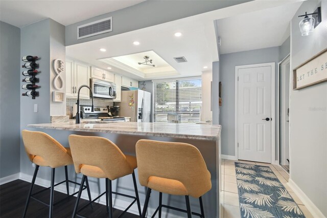 kitchen with appliances with stainless steel finishes, a kitchen bar, white cabinetry, and kitchen peninsula