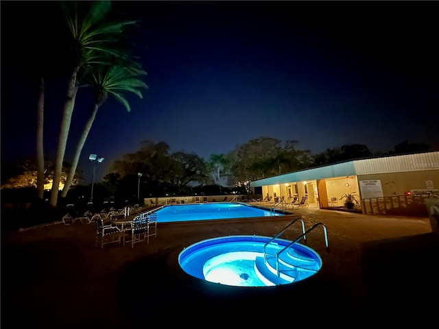 pool at night featuring a hot tub and a patio area