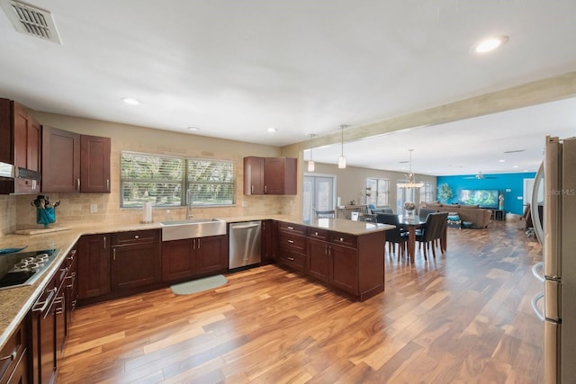 kitchen with pendant lighting, light hardwood / wood-style flooring, kitchen peninsula, sink, and appliances with stainless steel finishes